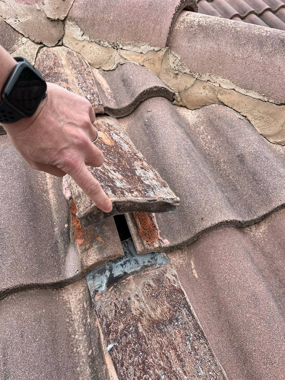 Technician pointing to a cracked and lifted roof tile during a storm damage inspection